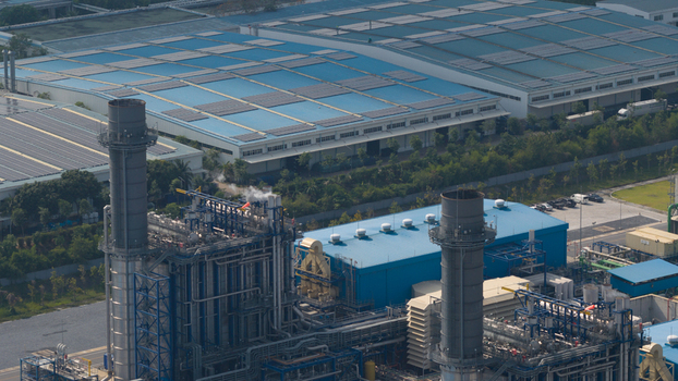 Aerial view of the industrial power plant facility with tall chimneys and large blue roofed warehouses in the industrial zone of Map Yang Phon Rayong Thailand.