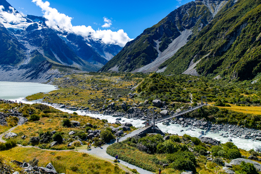 View of a glacial river winding through a golden valley towards snow capped mountains under a vibrant blue sky framed by rugged terrain Mount Cook Canterbury Region New Zealand. View of a glacial river winding through a golden valley towards snow capped mountains under a vibrant blue sky framed by rugged terrain Mount Cook Canterbury Region New Zealand.