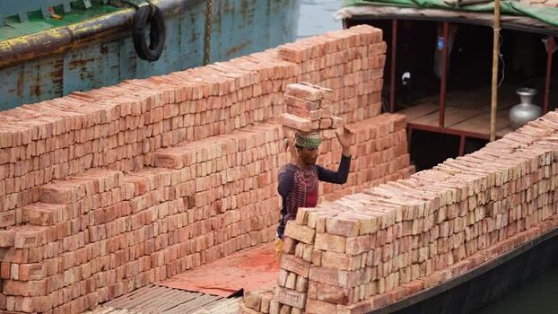 View of a worker carrying bricks on a boat in Aminbazar Bangladesh. View of a worker carrying bricks on a boat in Aminbazar Bangladesh.