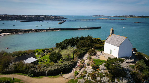 Aerial view of a white chapel sitting atop a rocky outcrop overlooking the serene turquoise sea with a distant pier stretching into the horizon Roscoff Brittany France. Aerial view of a white chapel sitting atop a rocky outcrop overlooking the serene turquoise sea with a distant pier stretching into the horizon Roscoff Brittany France.
