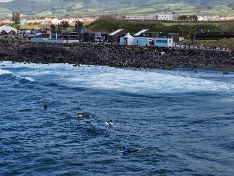 Aerial view of surfers waiting for waves near the rocky coast of Praia do Areal de Santa Barbara with green hills in the background Ribeira Grande Acores Portugal. Aerial view of surfers waiting for waves near the rocky coast of Praia do Areal de Santa Barbara with green hills in the background Ribeira Grande Acores Portugal.