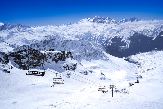 Aerial view of the La Rosiere ski resort featuring chairlifts over snow covered slopes and majestic alpine peaks under a clear blue sky in Montvalezan Auvergne Rhone Alpes France.