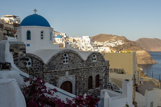 View of a traditional church with a blue dome and stone walls overlooking the sea in Santorini Greece.