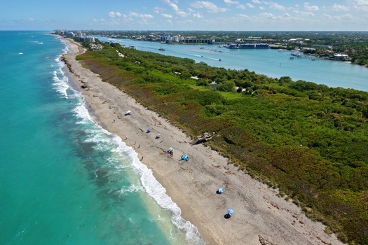 Aerial view of the turquoise coastline and sandy beach with umbrellas bordering lush green vegetation and the Jupiter Inlet Jupiter Florida United States. Aerial view of the turquoise coastline and sandy beach with umbrellas bordering lush green vegetation and the Jupiter Inlet Jupiter Florida United States.