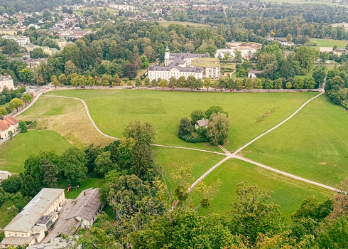 View of a large green meadow with intersecting walking paths a small house surrounded by trees and historic buildings in the background Salzburg Salzburg Austria. View of a large green meadow with intersecting walking paths a small house surrounded by trees and historic buildings in the background Salzburg Salzburg Austria.