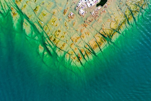 Aerial view of Jamaica Beach featuring flat rock formations and crystal clear turquoise water in Sirmione Lombardia Italy.