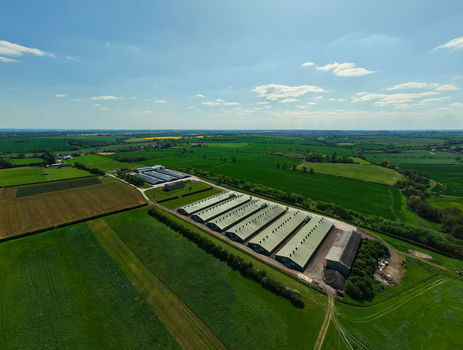 Aerial view of large agricultural farm buildings and livestock sheds surrounded by lush green fields and rural countryside under a clear blue sky in Kettering England United Kingdom. Aerial view of large agricultural farm buildings and livestock sheds surrounded by lush green fields and rural countryside under a clear blue sky in Kettering England United Kingdom.
