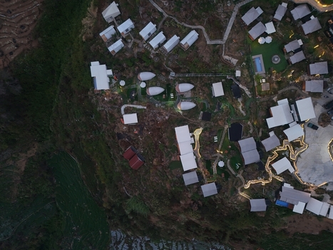 Aerial view of the Dieng resort area featuring modern cabins with white roofs winding pathways and terraced landscapes illuminated at dusk in Kejajar Central Java Indonesia. Aerial view of the Dieng resort area featuring modern cabins with white roofs winding pathways and terraced landscapes illuminated at dusk in Kejajar Central Java Indonesia.