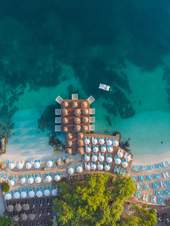 Aerial view of the Ksamil beach resort featuring a wooden pier with umbrellas turquoise water and sun loungers on the sandy shore Ksamil Vlore County Albania. Aerial view of the Ksamil beach resort featuring a wooden pier with umbrellas turquoise water and sun loungers on the sandy shore Ksamil Vlore County Albania.