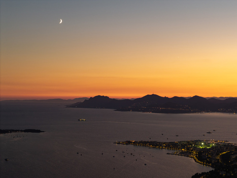 Aerial view of the coastline of Antibes at sunset with a crescent moon in the sky and city lights illuminating the harbor Antibes Provence Alpes Cote d Azur France. Aerial view of the coastline of Antibes at sunset with a crescent moon in the sky and city lights illuminating the harbor Antibes Provence Alpes Cote d Azur France.