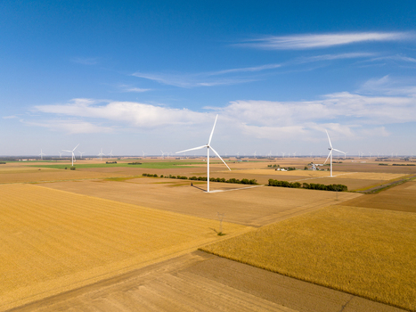 Aerial view of wind turbines in a vast golden agricultural field under a clear blue sky in Wolcott Indiana United States.