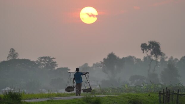 View of a man carrying baskets at sunset in Bogura Bangladesh. View of a man carrying baskets at sunset in Bogura Bangladesh.