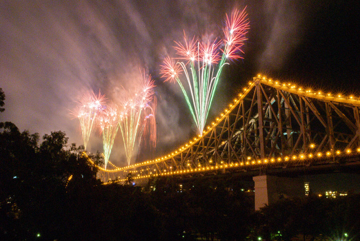View of the illuminated Story Bridge at night with vibrant fireworks bursting in the sky above the structure in Brisbane Queensland Australia.
