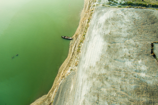 Aerial view of a small wooden boat moored on the sandy bank of a river in Rajshahi with textured riverbed patterns and calm green water Rajshahi Rajshahi Division Bangladesh.