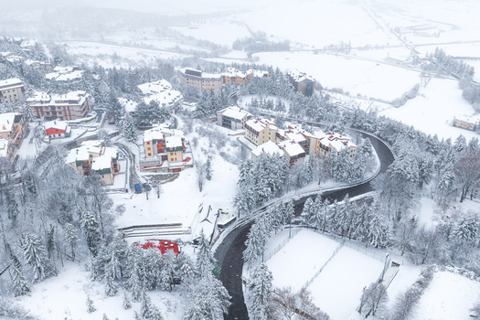 Aerial view of the snow covered town of Rivisondoli nestled in the mountains featuring winding roads evergreen trees and residential buildings in Rivisondoli Abruzzo Italy.