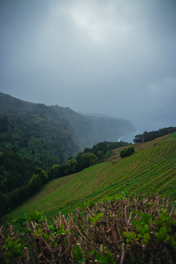 Aerial view of verdant slopes meet the rugged coastline under a moody sky contrasting textures and tones creating a dramatic landscape Ponta Delgada Azores Portugal.