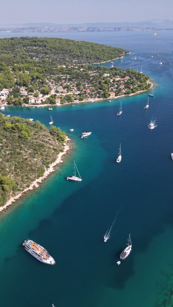 Aerial view of the turquoise waters of Necujam bay with sailboats and motorboats anchored near lush green hills and coastal houses Necujam Split Dalmatia County Croatia. Aerial view of the turquoise waters of Necujam bay with sailboats and motorboats anchored near lush green hills and coastal houses Necujam Split Dalmatia County Croatia.