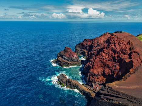 Aerial view of the rugged rust colored cliffs meeting the deep blue sea a stark contrast under the vast sky Capelo A&ccedil;ores Portugal.