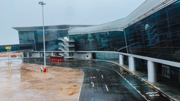 Bhogapuram India 22 August 2026 View of Alluri Sitarama Raju International Airport terminal building with modern glass facade wet tarmac and a red shuttle bus under an overcast sky. Bhogapuram India 22 August 2026 View of Alluri Sitarama Raju International Airport terminal building with modern glass facade wet tarmac and a red shuttle bus under an overcast sky.