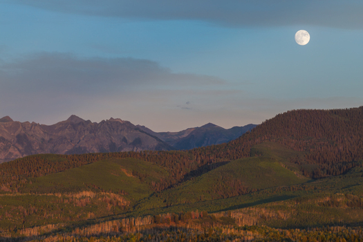 Aerial view of Mount Sneffels and the San Juan Mountain Range under a full moon with golden hour light illuminating the evergreen forests in Ouray Colorado United States. Aerial view of Mount Sneffels and the San Juan Mountain Range under a full moon with golden hour light illuminating the evergreen forests in Ouray Colorado United States.