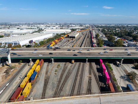 Aerial view of a busy railyard with colorful freight train cars parked on tracks beneath a highway overpass in an industrial area of Carson California United States.