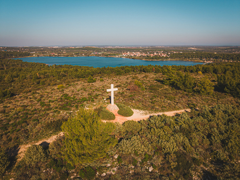 Aerial view of the stark white cross standing tall against the backdrop of the serene lake and verdant landscape Medulin Istria County Croatia.