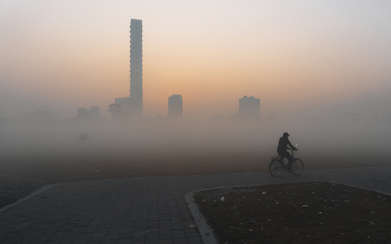 View of a lone cyclist braving the dense morning fog skyscrapers looming faintly in the distance under a pale ethereal sky Kolkata West Bengal India. View of a lone cyclist braving the dense morning fog skyscrapers looming faintly in the distance under a pale ethereal sky Kolkata West Bengal India.