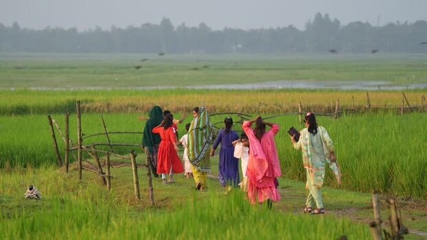 View of women and children walking through green fields Bangladesh.