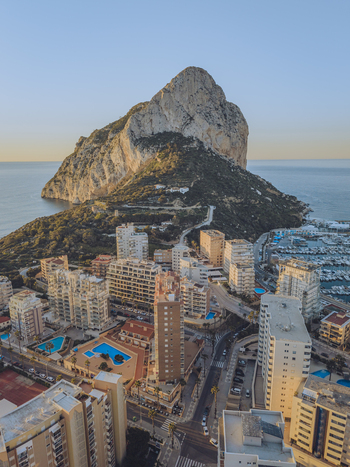 Aerial view of the Penon de Ifach mountain rising above the coastal town with high rise buildings swimming pools and the Mediterranean Sea Calp Valencian Community Spain. Aerial view of the Penon de Ifach mountain rising above the coastal town with high rise buildings swimming pools and the Mediterranean Sea Calp Valencian Community Spain.