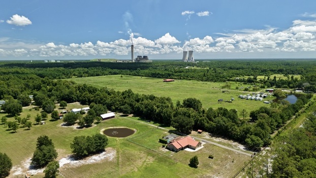 Aerial view of the Seminole Electric power plant with cooling towers and smokestacks rising above the surrounding lush green forest and rural landscape in Palatka Florida United States.