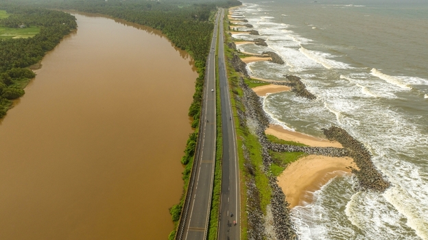 Aerial view of Maravanthe beach with a highway running between the Suparnika River and the Arabian Sea featuring rocky breakwaters and lush greenery in Maravanthe Karnataka India. Aerial view of Maravanthe beach with a highway running between the Suparnika River and the Arabian Sea featuring rocky breakwaters and lush greenery in Maravanthe Karnataka India.