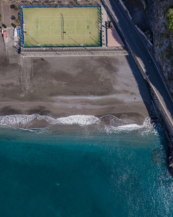 Aerial view of a tennis court nestled between a dark sandy beach and the turquoise sea alongside a road hugging the coastline Minori Campania Italy. Aerial view of a tennis court nestled between a dark sandy beach and the turquoise sea alongside a road hugging the coastline Minori Campania Italy.