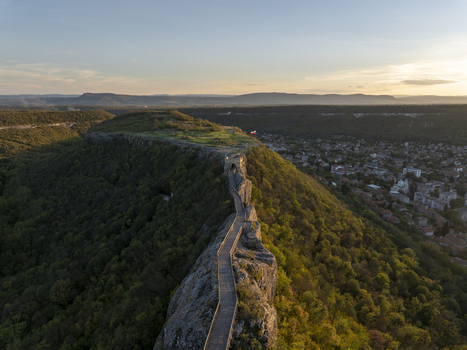 Aerial view of Ovech Fortress featuring a wooden walkway along the rocky ridge surrounded by lush green hills and the town of Provadia at sunset in Provadia Varna Bulgaria. Aerial view of Ovech Fortress featuring a wooden walkway along the rocky ridge surrounded by lush green hills and the town of Provadia at sunset in Provadia Varna Bulgaria.