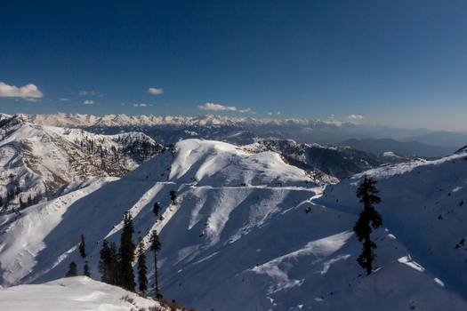 View of sunlight kissing snow capped peaks casting long shadows across the landscape with evergreens standing tall against the bright sky Haveli Azad Kashmir Azad Kashmir Pakistan.