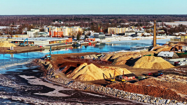 Aerial view of a timber yard with large piles of wood chips and industrial machinery situated along a frozen riverbank near a small town in LATVIA. Aerial view of a timber yard with large piles of wood chips and industrial machinery situated along a frozen riverbank near a small town in LATVIA.