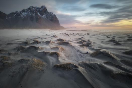 Aerial view of Stokksnes beach featuring black sand dunes and the majestic Vestrahorn mountain under a soft sunset sky with a photographer Sveitarfelagid Hornafjordur Iceland.