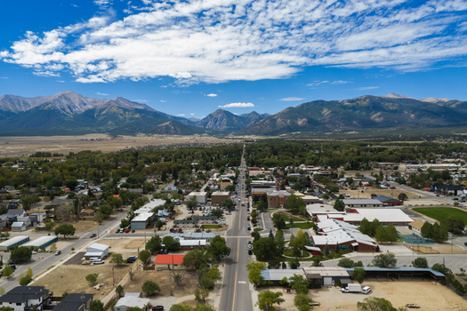 Aerial view of Collegiate Peaks towering over the town of Buena Vista with its grid of streets residential buildings and trees under a blue sky in Buena Vista Colorado United States.