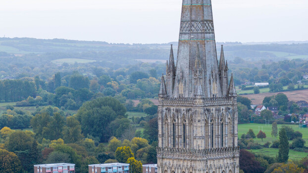 Aerial view of the iconic Salisbury Cathedral spire rising above the surrounding green landscape and urban rooftops in Salisbury Wiltshire United Kingdom. Aerial view of the iconic Salisbury Cathedral spire rising above the surrounding green landscape and urban rooftops in Salisbury Wiltshire United Kingdom.