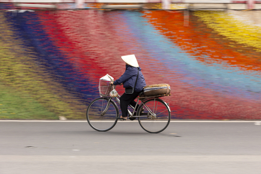 View of a person wearing a conical hat riding a bicycle past the colorful Ceramic Mosaic Mural in Hanoi Ha Noi Vietnam.