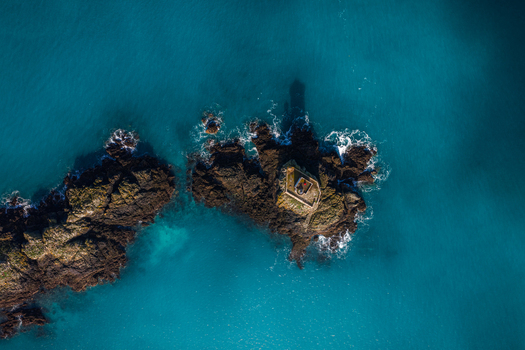 Aerial view of the Phare de L Ost Pic lighthouse perched on dark rocky reefs surrounded by vibrant turquoise sea water in Plouezec France. Aerial view of the Phare de L Ost Pic lighthouse perched on dark rocky reefs surrounded by vibrant turquoise sea water in Plouezec France.