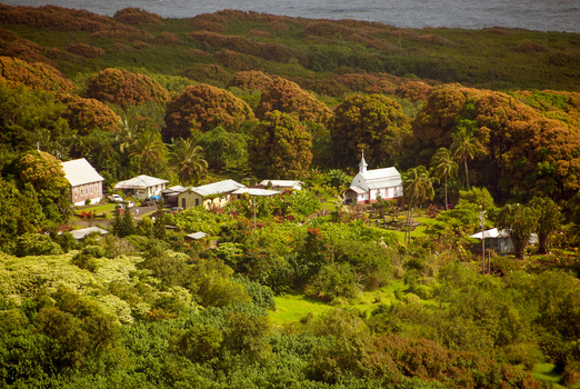 View of the historic church in Maui surrounded by lush tropical vegetation and dense forest with the ocean in the background in Maui County Hawaii United States.