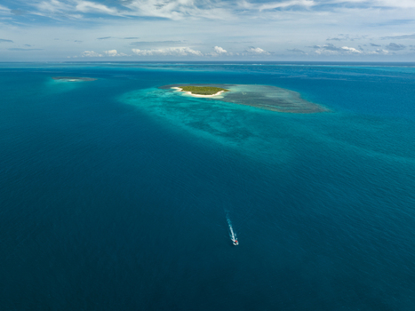 Aerial view of a pristine island surrounded by turquoise waters and a lone boat cutting through the deep blue sea Noumea New Caledonia. Aerial view of a pristine island surrounded by turquoise waters and a lone boat cutting through the deep blue sea Noumea New Caledonia.