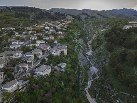 Aerial view of the historic stone houses of Gjirokaster nestled on a hillside overlooking a deep rocky gorge with lush greenery and mountains Gjirokaster Gjirokaster County Albania. Aerial view of the historic stone houses of Gjirokaster nestled on a hillside overlooking a deep rocky gorge with lush greenery and mountains Gjirokaster Gjirokaster County Albania.