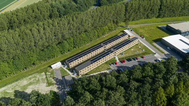 Aerial view of a modern residential complex with solar panels on the roofs surrounded by lush green trees and a parking area in Middenmeer North Holland Netherlands.