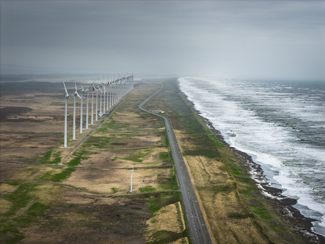Aerial view of a long row of wind turbines stretching along the coastline with a road running parallel to the sea in Wakkanai Hokkaido Japan.