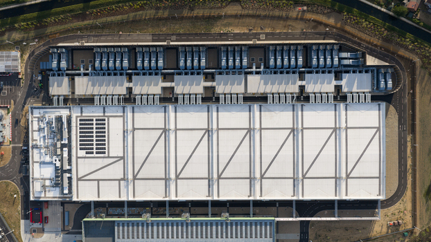 Aerial view of a large industrial data center facility with expansive white rooftops cooling units and surrounding paved access roads in Waltham Cross England United Kingdom.