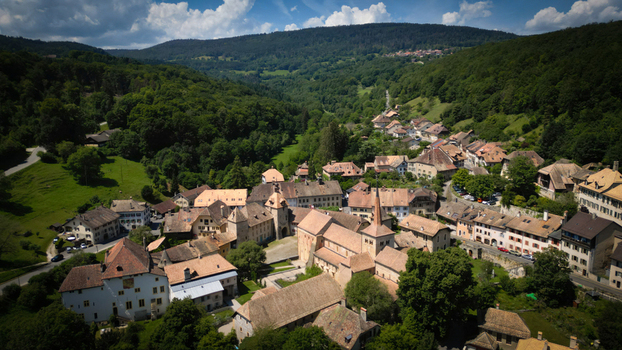 Aerial view of Romainm&ocirc;tier Abbey nestled amidst lush green valley a serene tapestry of terracotta roofs and stone buildings Romainm&ocirc;tier Envy Vaud Switzerland.