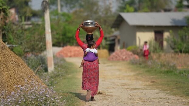 View of a woman carrying pots on her head and a child on her back Nepal. View of a woman carrying pots on her head and a child on her back Nepal.