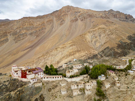Aerial view of Karsha Monastery perched on a rocky cliffside in the Zanskar Valley surrounded by rugged mountain slopes and scattered traditional white buildings in Zanskar Ladakh India.