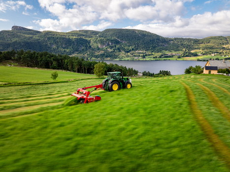 Aerial view of a tractor harvesting silage in a lush green field with mountains and a fjord in the background in Fister Rogaland Norway. Aerial view of a tractor harvesting silage in a lush green field with mountains and a fjord in the background in Fister Rogaland Norway.